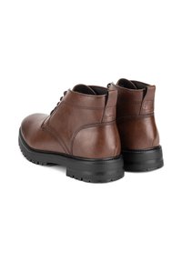 Hnědé kožené kotníkové boty s kulatými špičkami, černými gumovými podrážkami a jemnými detaily prošívání. Šňůrky upevňují přední část, což zajišťuje bezpečné obutí.