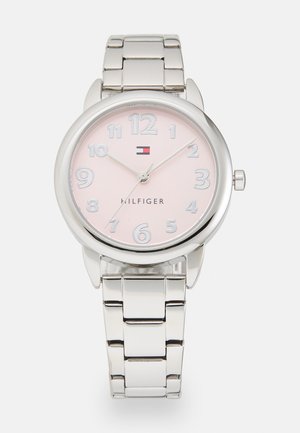 Relógio prateado com um caixa redonda, mostrador rosa claro, grandes números brancos e pulseira de metal. Apresenta logotipo e marcadores de horas simples.