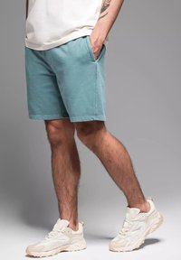 Shorts en coton bleu clair avec poches latérales, de longueur genou, associés à des baskets beiges avec des surfaces texturées et un design épuré.
