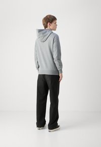 Felpa grigia con cappuccio, dotata di polsini e orlo a coste, abbinata a pantaloni neri larghi e scarpe da ginnastica nere. Design semplice, texture morbida.