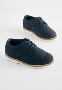 Chaussures brogues en cuir bleu marine avec des perforations, semelles en caoutchouc blanches et lacets gris. Design classique avec un bout arrondi.