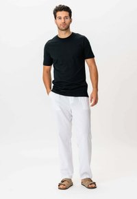 Sort kortærmet t-shirt, hvide linnedbukser med lommer og brune sandaler med spænde detalje. Afslappet, let outfit.