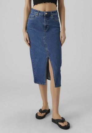 Femme portant une jupe midi en denim bleu taille haute avec une fente sur le devant, un top court noir et des sandales à plateforme noires.