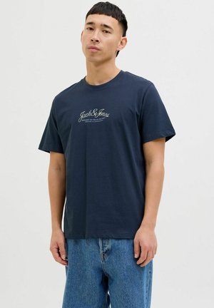 Navy blue cotton t-shirt with short sleeves, featuring a subtle white logo in cursive on the chest and a relaxed fit.
