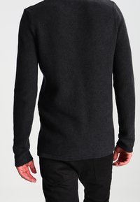 Maglione lungo a maniche lunghe nero lavorato a maglia con un motivo testurizzato. Orlo leggermente più lungo sul retro, con polsini aderenti e scollatura a girocollo.