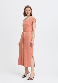 Roestkleurige maxi-jurk met een V-hals, korte mouwen, een tailleband en zijsplitten. Draag met zwarte hakken. Gladde katoenen stof.