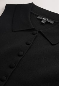 Top lavorato a maglia nero a maniche corte con colletto appuntito e bottoni rivestiti in tessuto sulla parte anteriore, marchiato NEXT, prodotto in Cina.