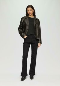 Zwarte leren motorjack met zilveren ritsen, zwarte getailleerde top, uitlopende zwarte jeans en puntige zwarte enkellaarsjes.