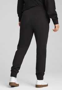 Svarta sweatpants med elastiskt midjeband och manschetter, med slät tyg och avslappnad passform. Matchas med vita sneakers.