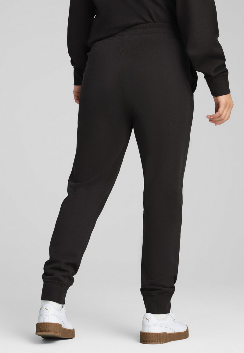 Pantaloni della tuta neri con vita e polsini elastici, realizzati in tessuto morbido e dalla vestibilità rilassata. Abbinati a sneakers bianche.