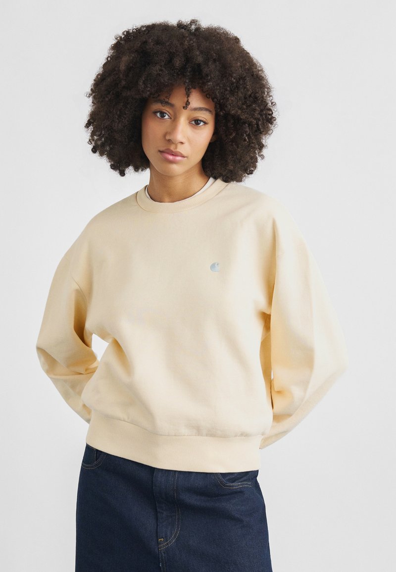 Φούτερ σε ανοιχτό μπεζ βαμβάκι με μακριά, χαλαρά μανίκια, ριμπ λαιμόκοψη και στρίφωμα. Διαθέτει μικρό λογότυπο στο στήθος.