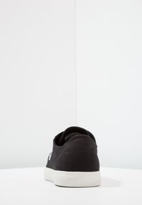 Baskets en toile noire avec semelle en caoutchouc blanche. Design simple avec une finition texturée et un logo contrastant.