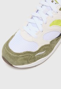 Tenisi cu un superior din suede verde și crem, panouri din plasă texturizată, șireturi albe și o talpă din cauciuc. Prezintă un model distinctiv pe lateral.