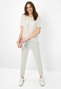 T-shirt à rayures crème clair associé à un pantalon slim gris clair et des baskets blanches, tenant une pochette argentée brillante. Textures de tissu lisses.