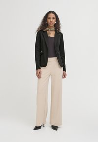 Černý blazer, přiléhavý, z lehkého materiálu; fialový top, měkká textilie; béžové široké kalhoty, hladký materiál; černé lodičky, špičatá špička.