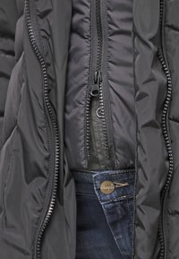 Chaqueta negra acolchada con doble cremallera y forro interior suave. Combinada con jeans de mezclilla oscuros que presentan un acento de botón metálico.
