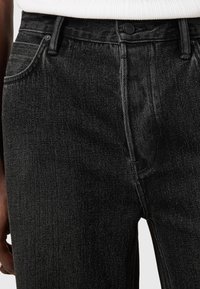 Schwarze Denim-Jeans im Slim-Fit, mit einem Knopfverschluss, vorderen Taschen und Kontrastnähten entlang der Nähte. Glatte Textur.
