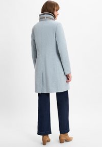 Lichtblauwe wollen jas met een hoge kraag en een gestructureerde stof. Heeft een rechte snit, lange mouwen en een achterste split voor meer bewegingsvrijheid.