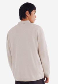 Helle beige gestrickte Pullover mit einem Kragenhals, lockerer Passform, langen Ärmeln und einer weichen Textur, von hinten gezeigt.