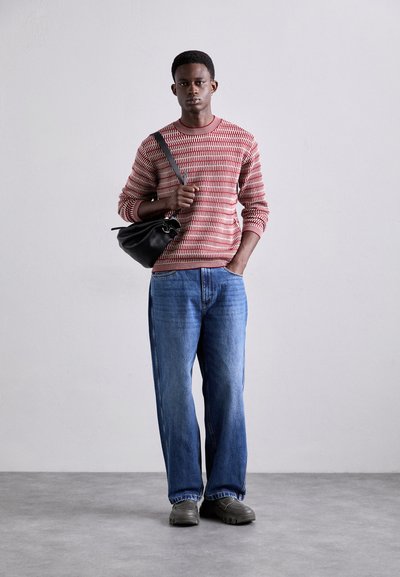 Pull rouge et blanc à motifs, jeans bleus larges et sac noir. Texture douce, design décontracté et tissu lisse pour les chaussures.