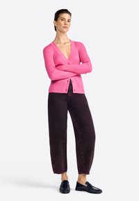 Cardigan ajusté rose à côtes avec des manches longues et des boutons, associé à un pantalon baggy violet foncé et des mocassins noirs. Design simple et moderne.