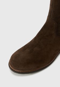 Bruine suède laars met een ronde neus, een gladde textuur en een bruine rubberen zool. Heeft minimale stiksels en een slanke silhouette.