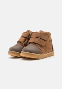 Stivaletti per bambini in suede e pelle marrone con due cinturini in velcro, punta arrotondata, suola in gomma e cuciture dettagliate. Parte superiore testurizzata e design resistente.