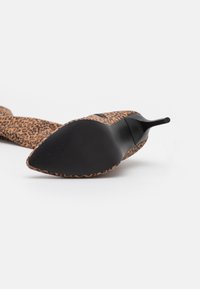 Zapato de tacón alto con estampado de leopardo, punta afilada, suela negra y tela texturizada para agarre. Presenta un diseño elegante y un tacón pronunciado.