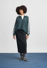 Tyrkysová fleecová mikina s bílými akcenty a třemi pruhy, doplněná černou midi sukní a šedými sportovními botami.