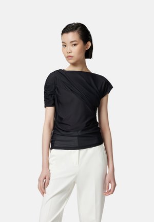 Top nero drappeggiato con maniche a sbuffo corte, caratterizzato da una texture liscia e un ampio scollo, abbinato a pantaloni bianchi su misura.