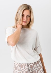 Lichtbeige, losse gebreide top met korte mouwen, met een zachte textuur. In combinatie met een gestreepte lichtroze rok met geometrisch ontwerp.
