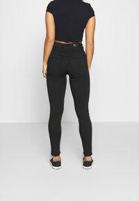 Svarta tajta jeans med hög midja och bakfickor, tillsammans med en svart kortärmad tröja och svarta sneakers. Slät tygtextur.