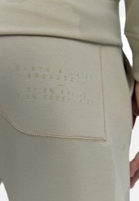 Leggings beige clair avec une poche texturée comportant des inscriptions en relief détaillant la composition de l'eau : 97,5 % saline, 2,5 % d'eau douce.