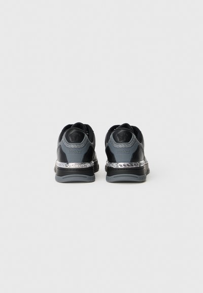 Black athletic shoes with a textured back, silver accents, and a contrasting logo. Features a unique design with a thick sole and decorative band.