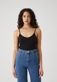 Svart ermeløs bodysuit med V-hals, kombinert med blå jeans med spredte hvite dekorasjoner og høy liv.