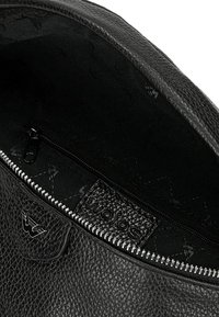Interno di una borsa a tracolla in pelle nera con una texture liscia, chiusura con zip e un sottile dettaglio del logo del marchio. Presenta un ampio scomparto foderato.