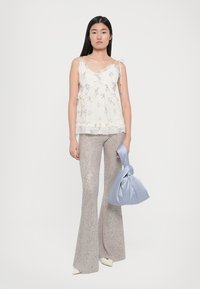 Camisola a stampa floreale con spalline regolabili e rouches sovrapposte. Pantaloni a zampa d'elefante argentati con paillettes lucide. Borsa annodata blu chiaro. Scarpe bianche con tacco.
