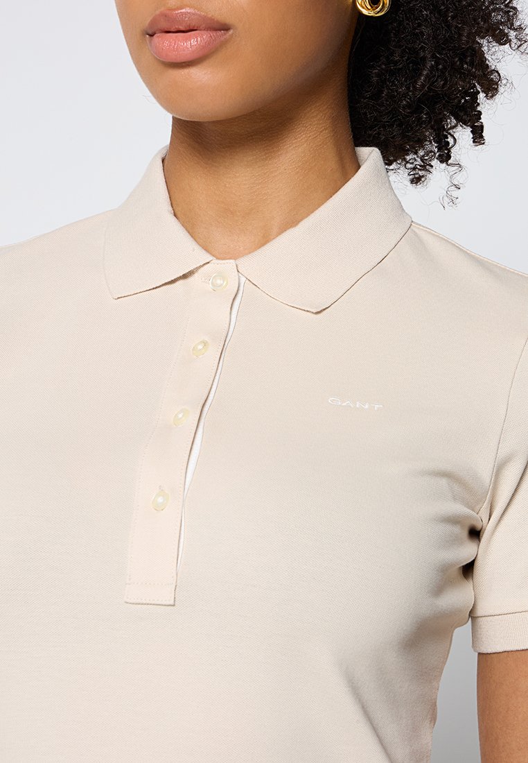 Beige Polo-Shirt aus strukturiertem Stoff, mit klassischem Kragen, kurzen Ärmeln und Knopfleiste. Enthält subtile Logodetails.