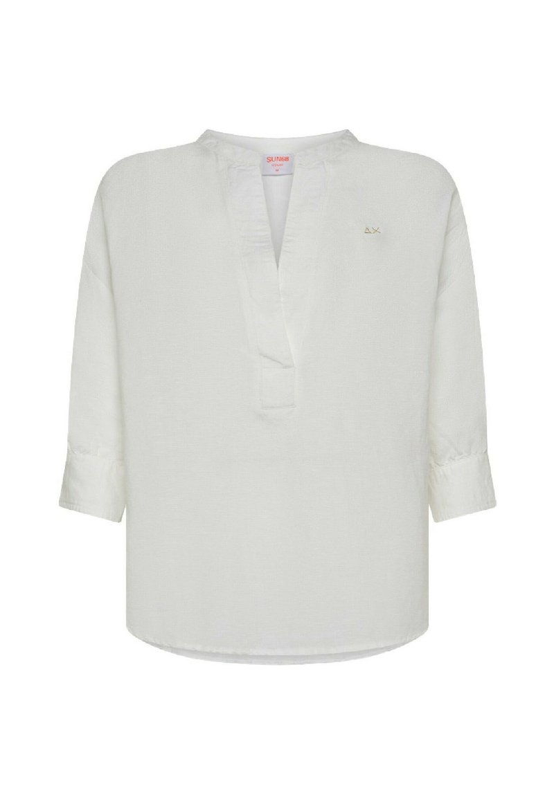 Camicia tunica bianca in lino con scollatura a V, maniche lunghe e orlo leggermente curvo. Presenta un piccolo logo dorato sul lato sinistro.