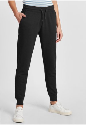 Sorte joggebukser med snor i livet, sidelommer og smale ben. Materialet ser mykt og litt strukturert ut. Kombinert med hvite joggesko.