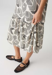 Black and white patterned dress with flared hem and gathered details, paired with black mesh Mary Jane shoes featuring a strap and buckle.