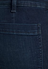 Mörkblå denimjeans som visar en bakficka med en överstickad design, med en texturerad yta och rena sömdetaljer.