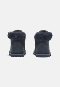 Botas azul marino con un acabado en ante texturizado, con un borde de pelaje sintético en el puño y una suela de goma resistente, que incluye una cremallera lateral.