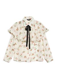 Blusa floral em creme com rosas cor-de-rosa, apresentando um grande colarinho de folhos e um laço preto no pescoço. Mangas compridas com punhos de botão.