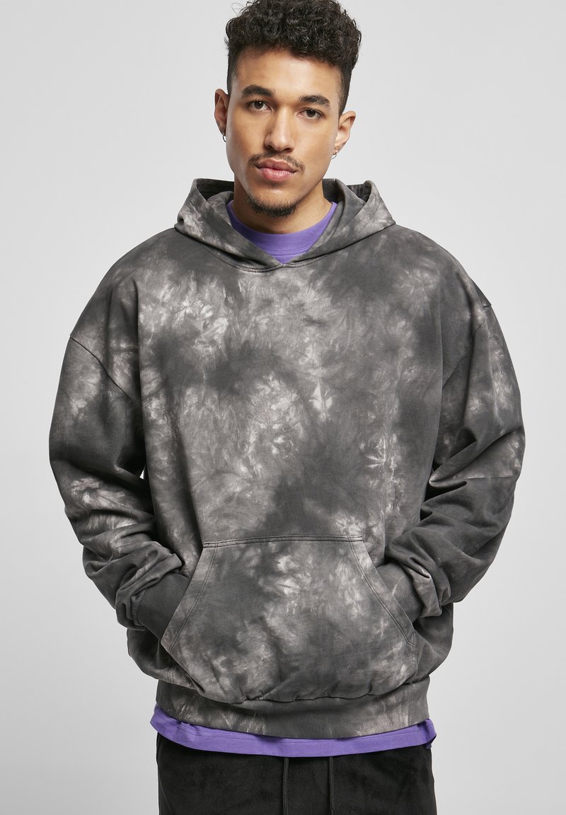 Sivi hoodie s uzorkom od batik boje s prednjim džepom, velikom kapom i rebrastim manžetama, složen preko ljubičaste majice, prikazan na neutralnoj pozadini.