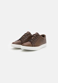 Baskets en cuir marron avec une texture lisse, dotées de lacets noirs, d'une semelle en caoutchouc blanche et d'un logo discret sur la languette.