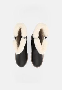 Schwarze Lederstiefel mit cremefarbenem Fellfutter, abgerundeter Form und flacher Sohle. Die Fellmanschette ist deutlich sichtbar. Keine sichtbaren Beschläge.