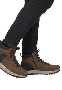Botas de senderismo de cuero marrón con acentos negros, diseño de cordones, tejido texturizado y detalle de cremallera lateral. Suela de goma con patrón de tachuela.