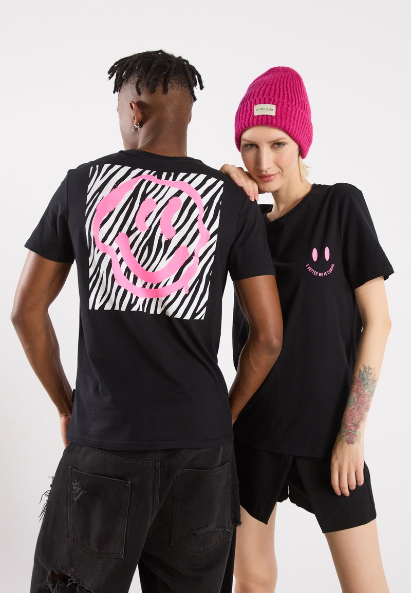 Svarte t-skjorter med rosa smiley-grafikk; en av dem har zebra-striper. En modell har på seg en rosa lue, noe som gir tekstur og fargekontrast.