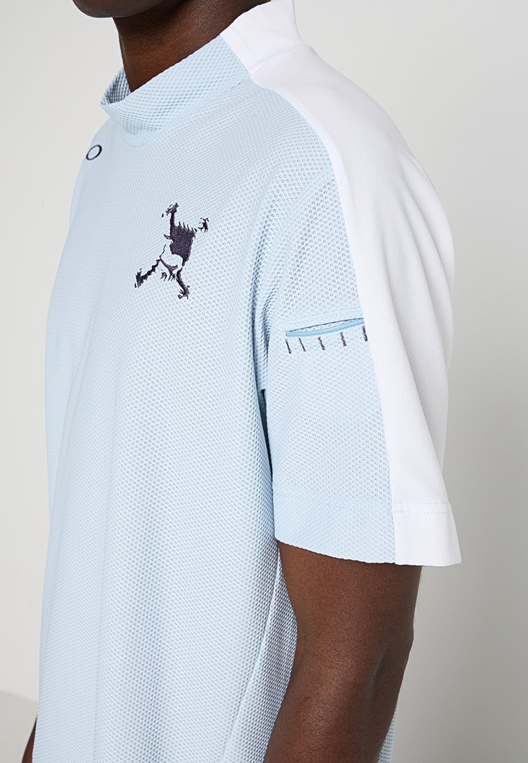 Hellblaues, kurzärmliges Poloshirt mit Mesh-Textur, weißen Akzenten und einem gestickten Logo auf der Brust. Auffälliges Detail an den Ärmeln mit blauen Nähten.